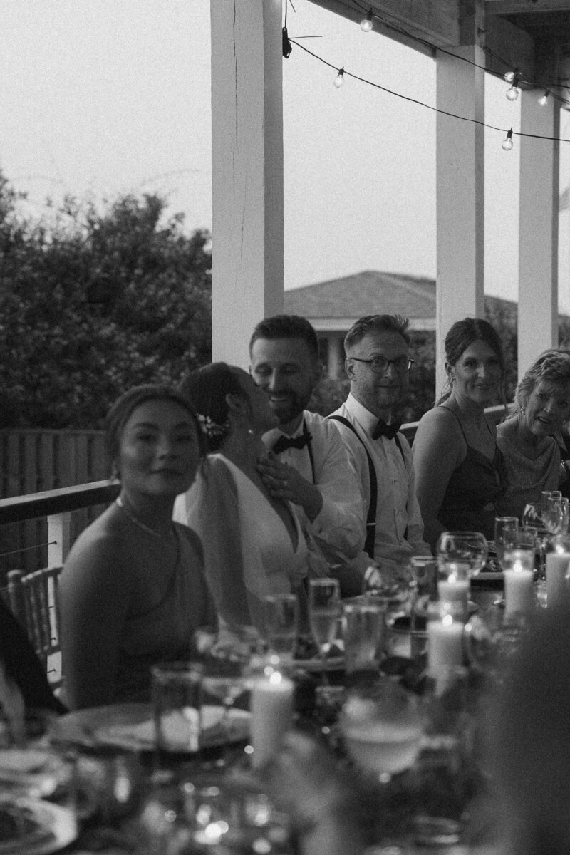 Black and white photo of wedding guests at a table, focus on a couple