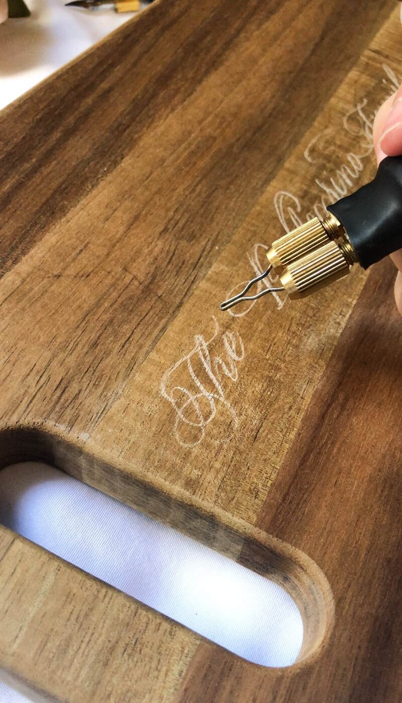 calligraphy chalk draft on a charcuterie board right before the wood burning tool heats it