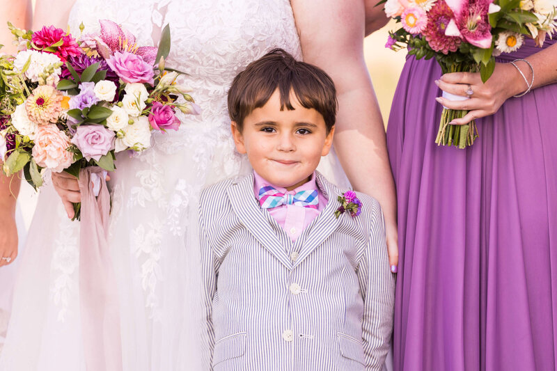 Boy wearing suit and a boutonniere standing in front of woman in bridal gown holding bouquet