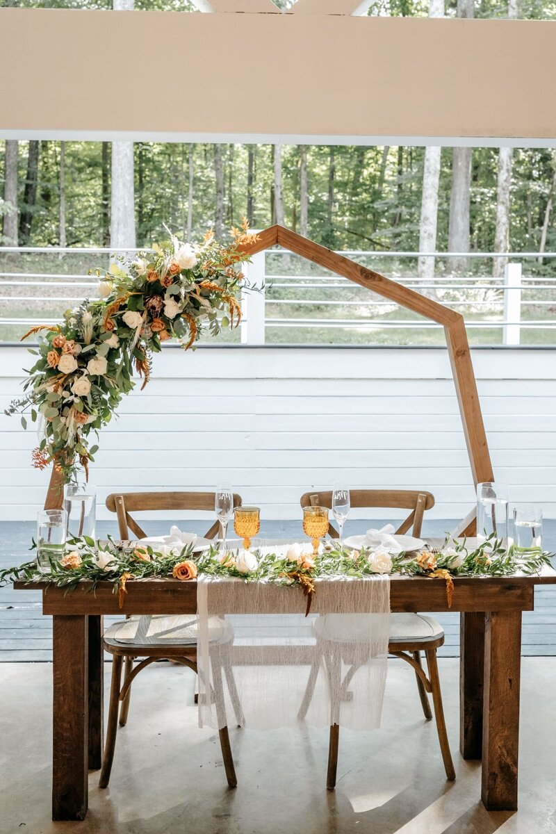 Flowers on Sweetheart table with geometrical arbor behind, reception at Firefly Lane