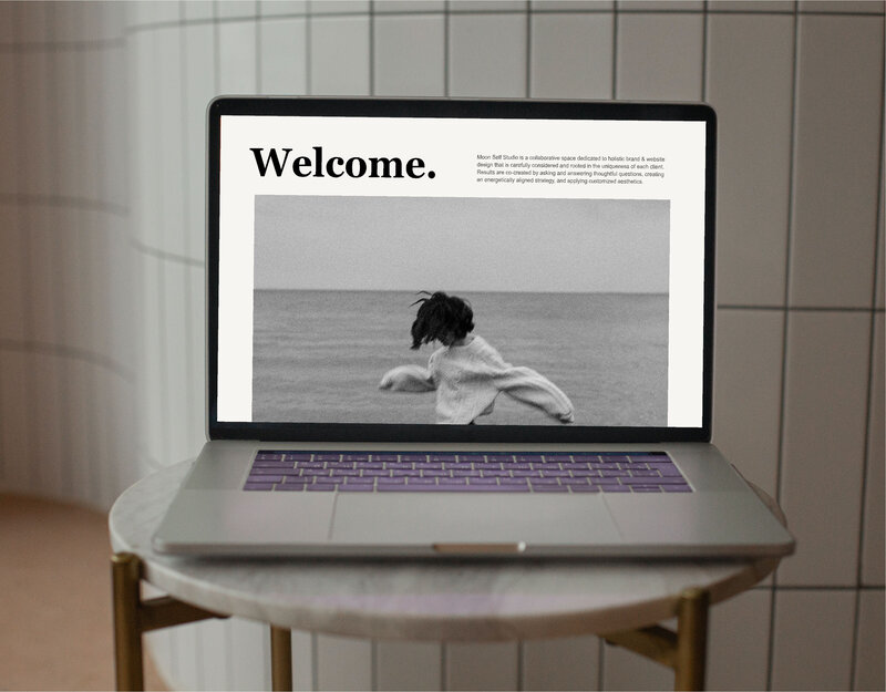White tile background with laptop open to a modern minamalist editorial style website design by Stephanie Thornton at The Tenth House