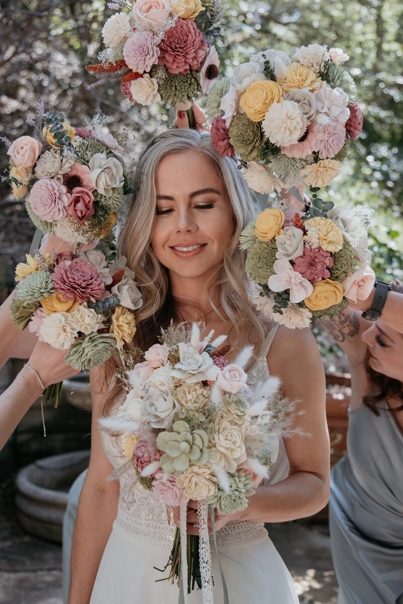 bride stands with bouquet and eyes closed as bridesmaids hold their bouquets around her head