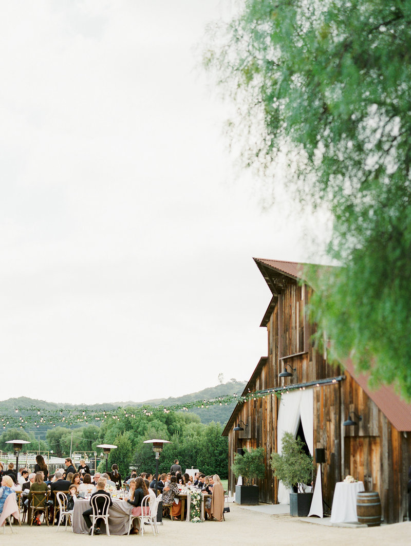 Wedding reception dinner next to a brown barn with string lights overhead and twinkle lights  setting the mood at greengate ranch and vineyard