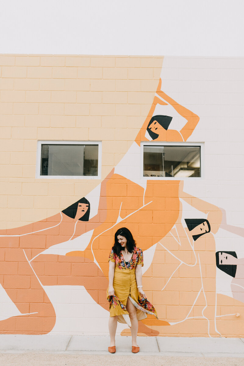 Amber wearing yellow skirt and floral top in front or orange abstract art, Austin branding, family and wedding photographer