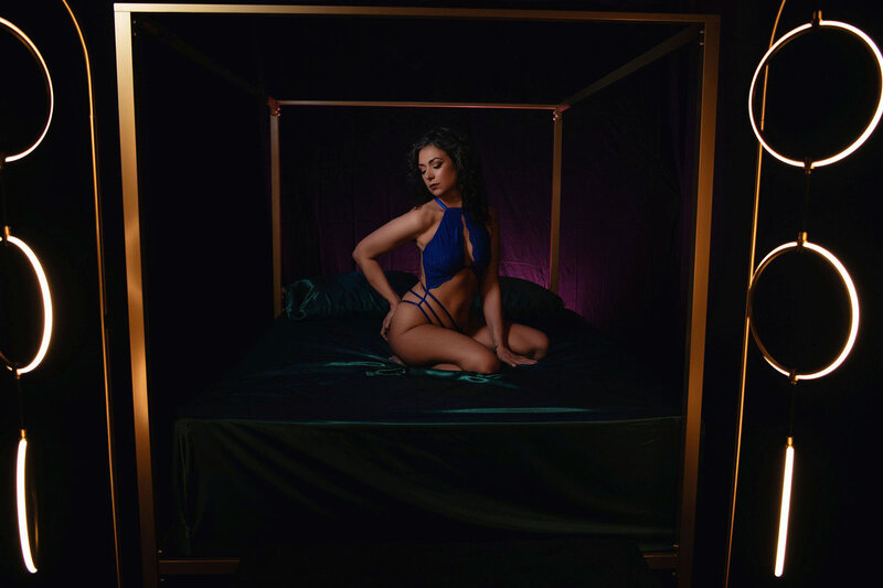 Low light boudoir photo of woman kneeling on bed
