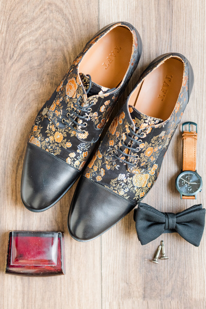 Detail photograph of a groom's fancy shoes, watch, bowtie and cufflinks on a wood background.