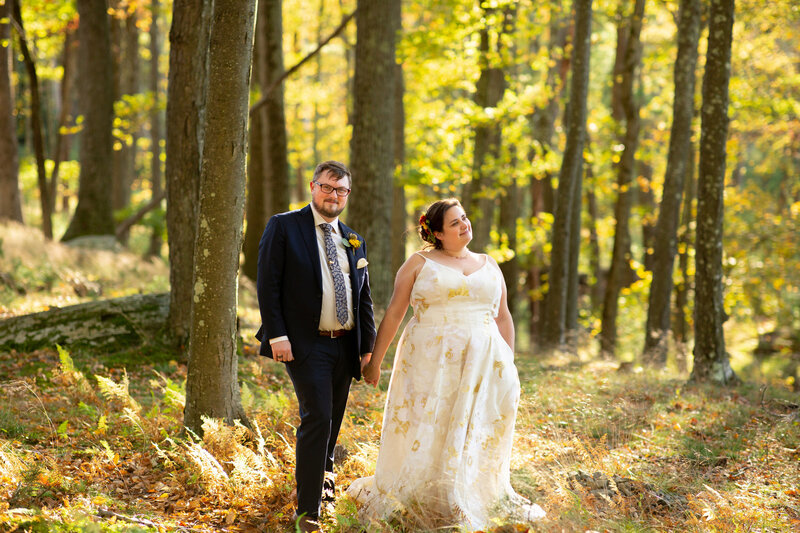 A bride and groom smiling and holding hands in a forest.