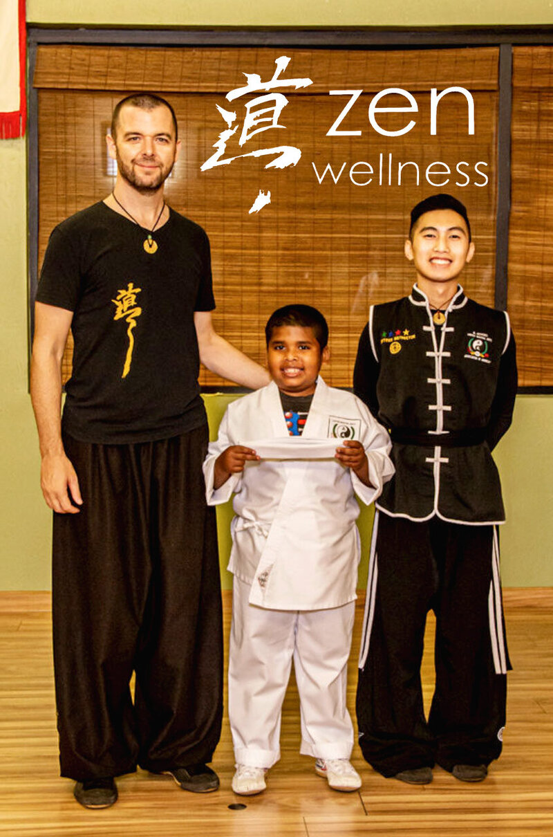 Instructors Jason Campbell and Allen standing on either side of young student holding belt and wearing gi while smiling