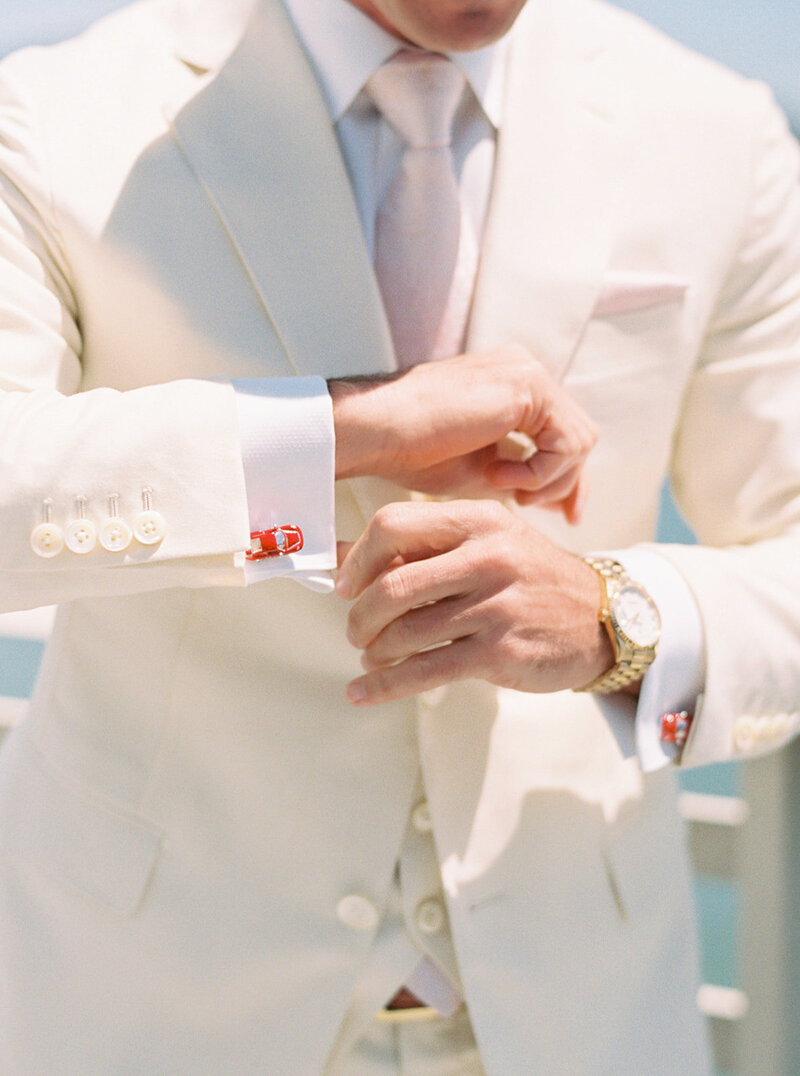 Close-up of groom adjusting vintage cufflinks in a cream suit, captured in editorial wedding photography style on the California coast.