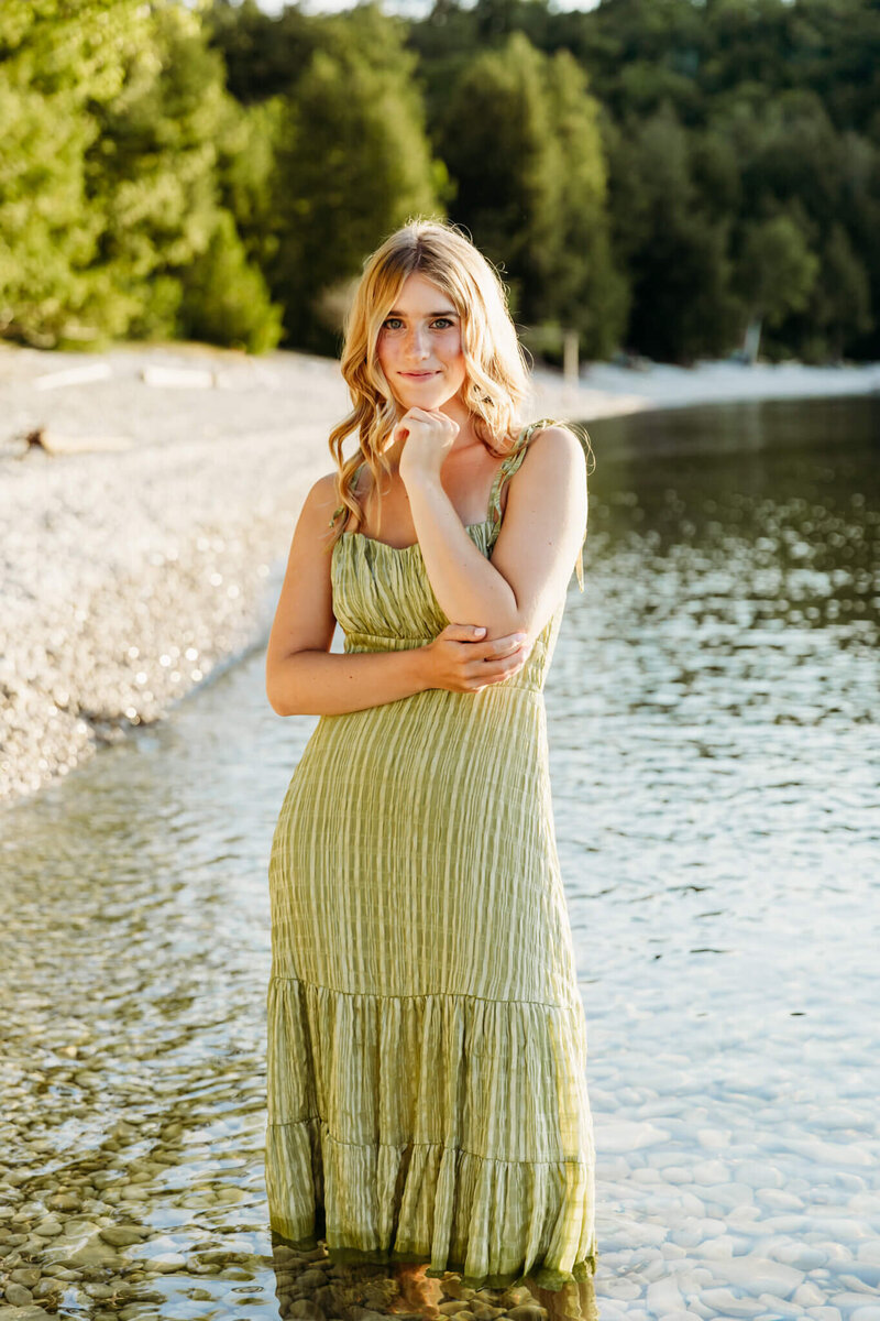 high school girl in a striped green dress standing in a clear lake in Door County for photo session