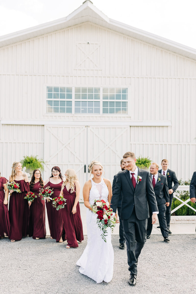 Bride and Groom walking in front of white barn with their wedding party at White Dove Barn