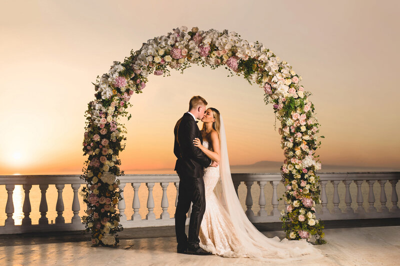 kevin de bruyne kissing his bride under a flower arch at sunset in sorrento