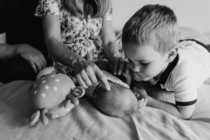 Newborn Photographers, two young siblings admire new baby on the bed
