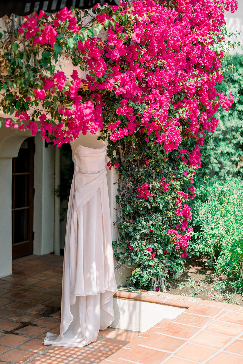 Wedding dress hanging beneath vibrant pink bougainvillea outside Hummingbird Nest Ranch in Simi Valley California