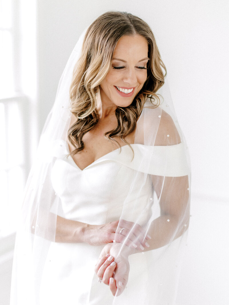 Portrait of a bride with brown curled hair and a veil draped around her shoulders