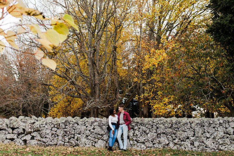 couple in front of stone wall and autumn leaves