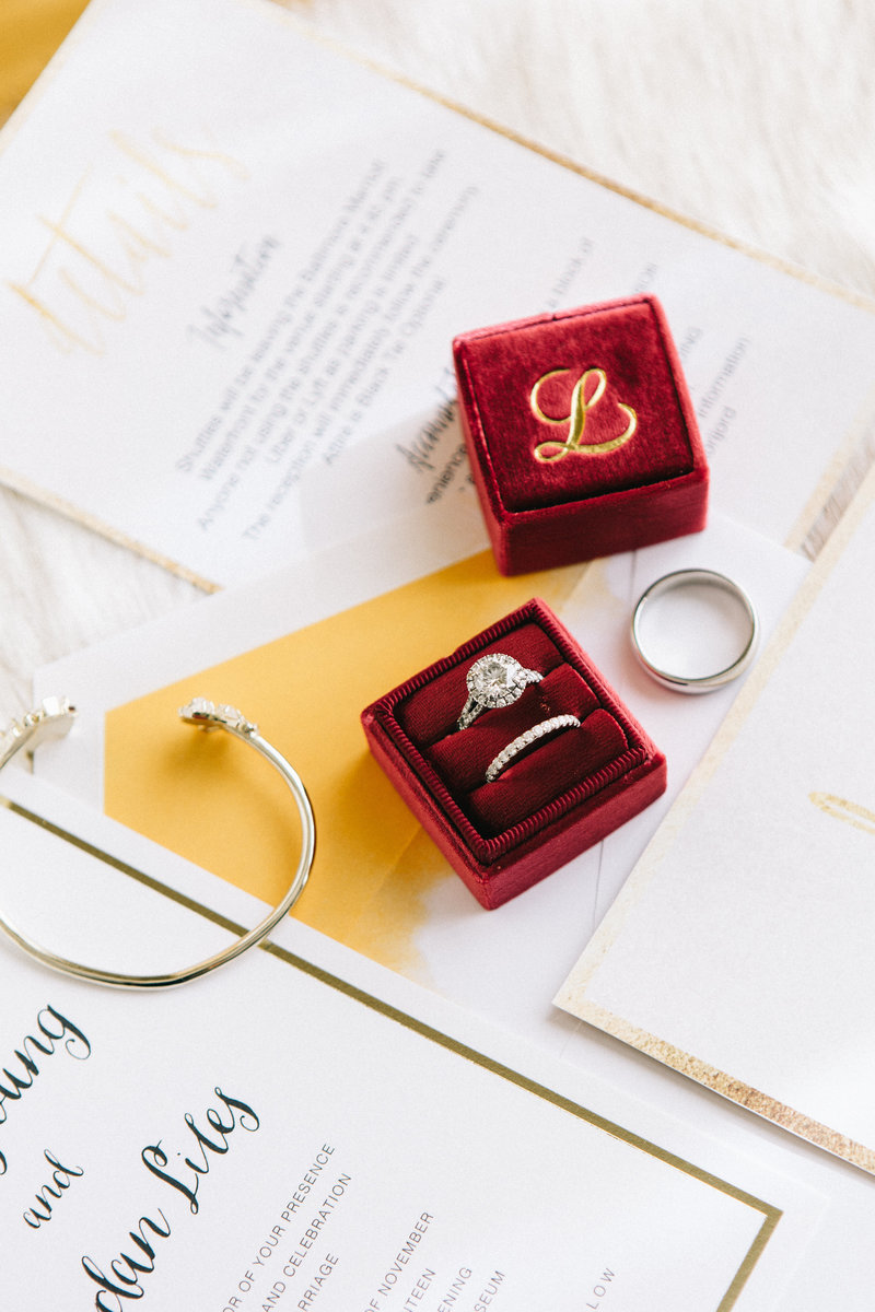 Cranberry ring box with wedding bands and gold details