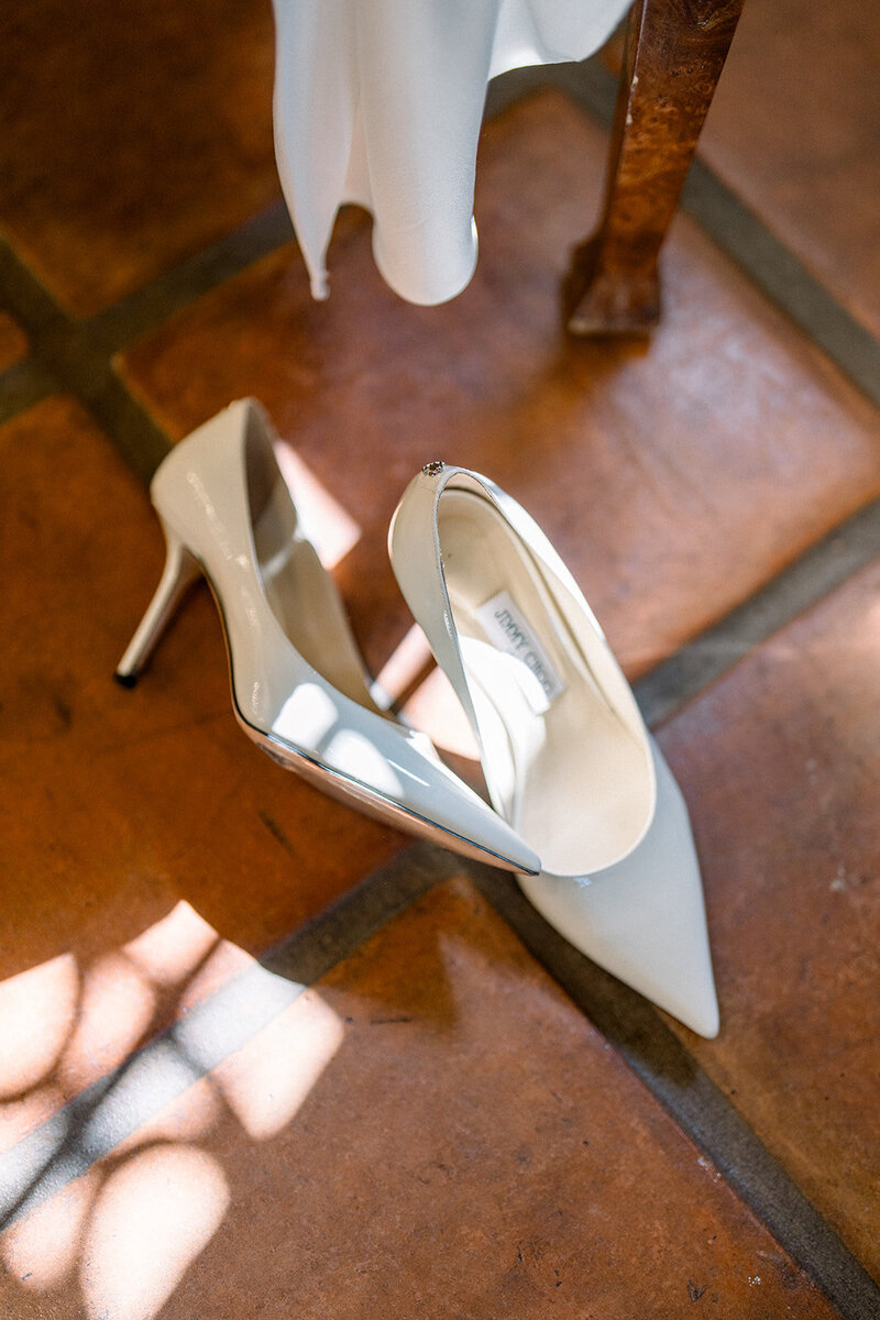 White bridal heels beneath silk gown hem on terracotta tile at a romantic wedding venue in Southern California