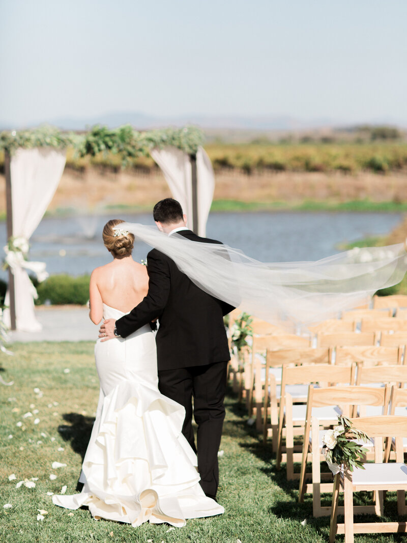 Bride and groom walking down outdoor ceremony aisle to lake
