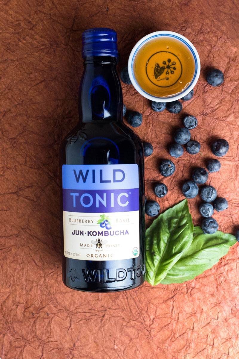 Bottle of wild tonic with blue berries and a dish of honey
