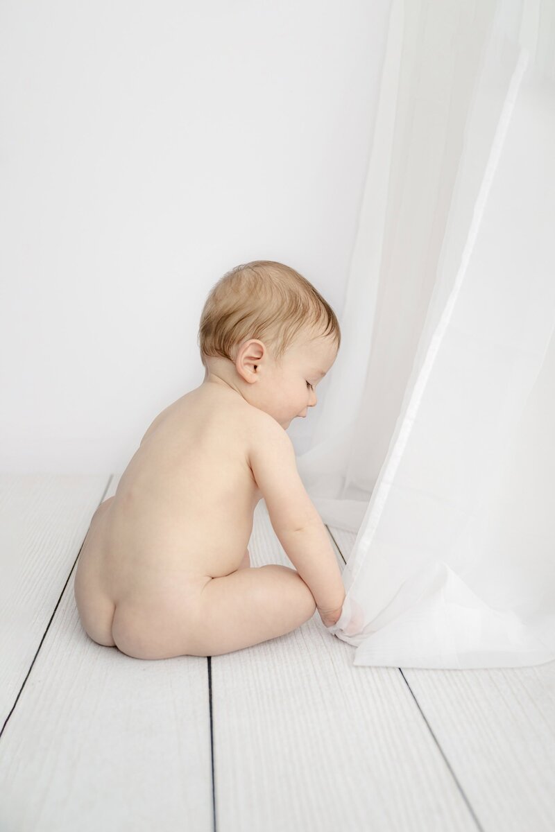 littel boy sits with out diaper in his seven month sitter session