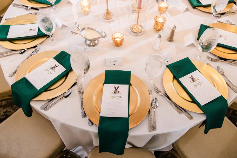 Elegant dining table setting with gold plates, green napkins, and menu cards for a formal event designed by a wedding coordinator in Iowa.