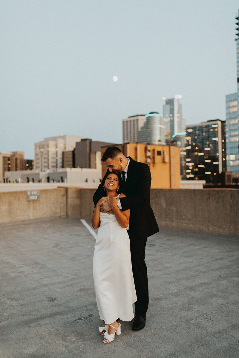 Elopement session at sunset on a rooftop, where the groom kisses the bride on the head and embraces her tenderly