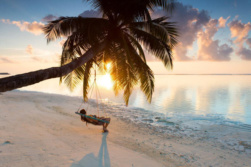 Woman sitting down on a hammock on a coconut tree with a beach view