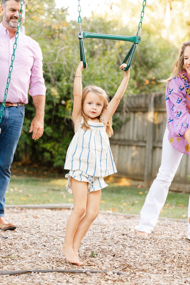 A mom and dad joyfully play with daughter on swing set.