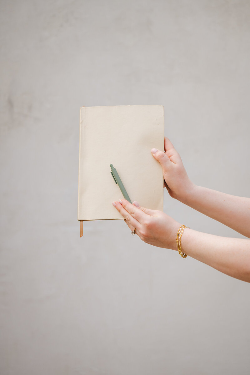 Woman's hands holding a tan notebook and green pen