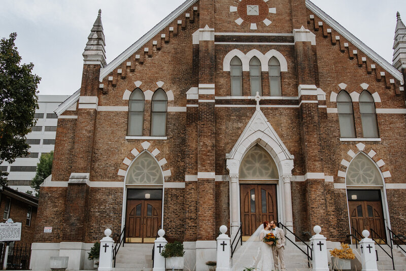 bride and groom kissing in front of large church with steeple