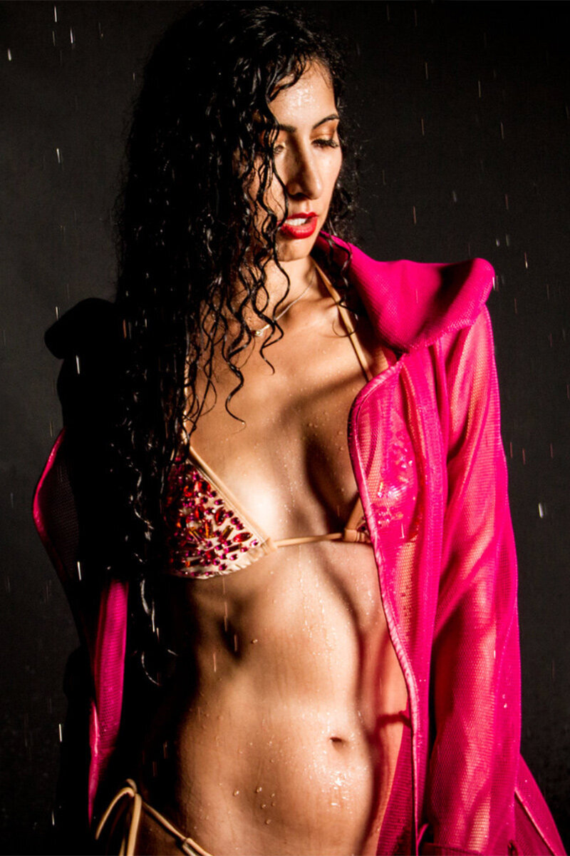 Female Personal Branding Image wearing patterned bikini and hot pink jacket hair wet black standing against backdrop