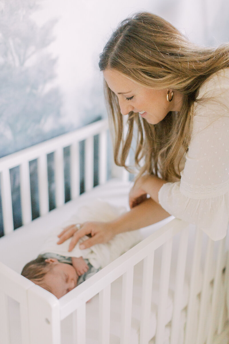 Mother leaning over crib with her hand on her newborn son
