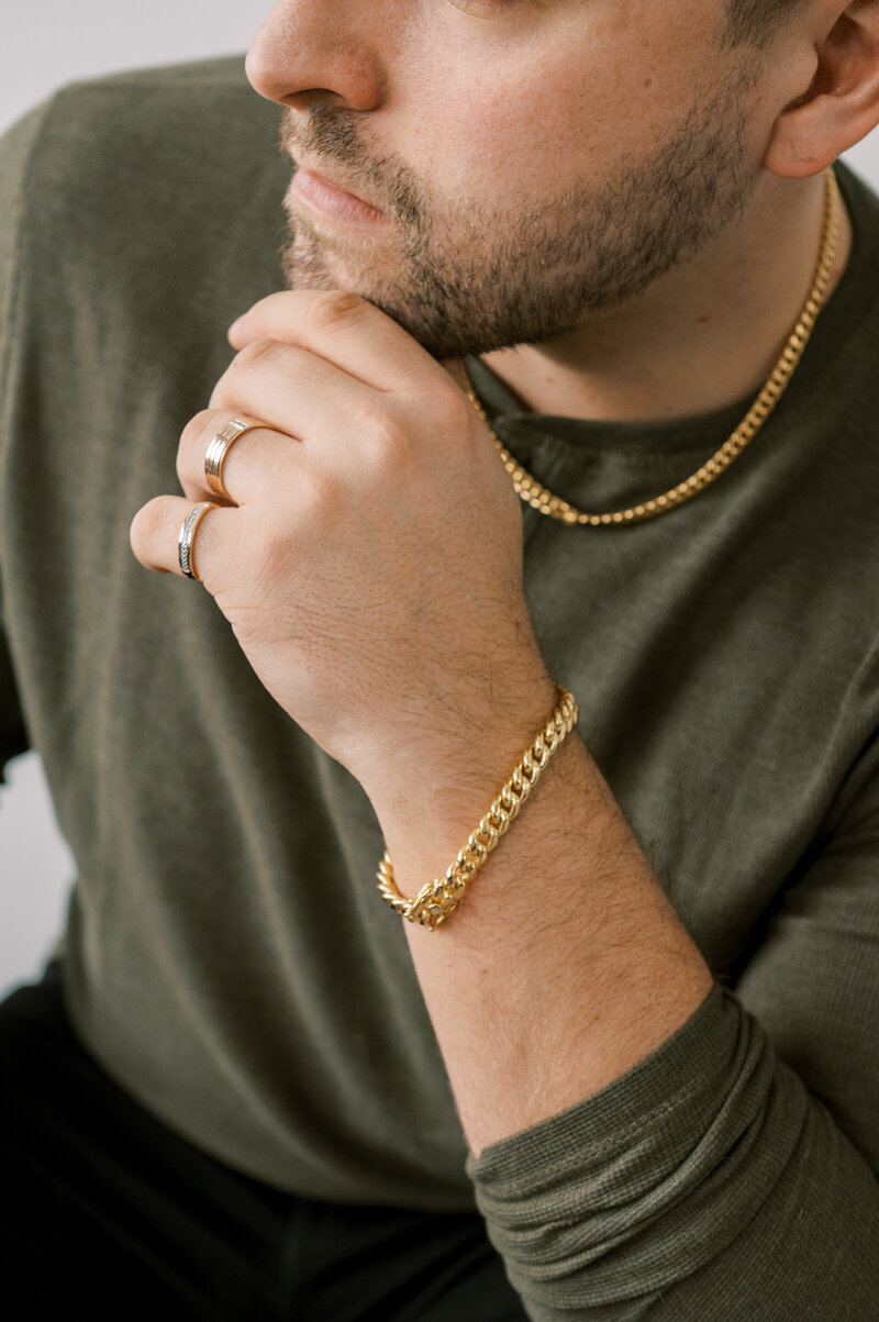 Upclose of man in green shirt wearing gold necklace, bracelet, and rings