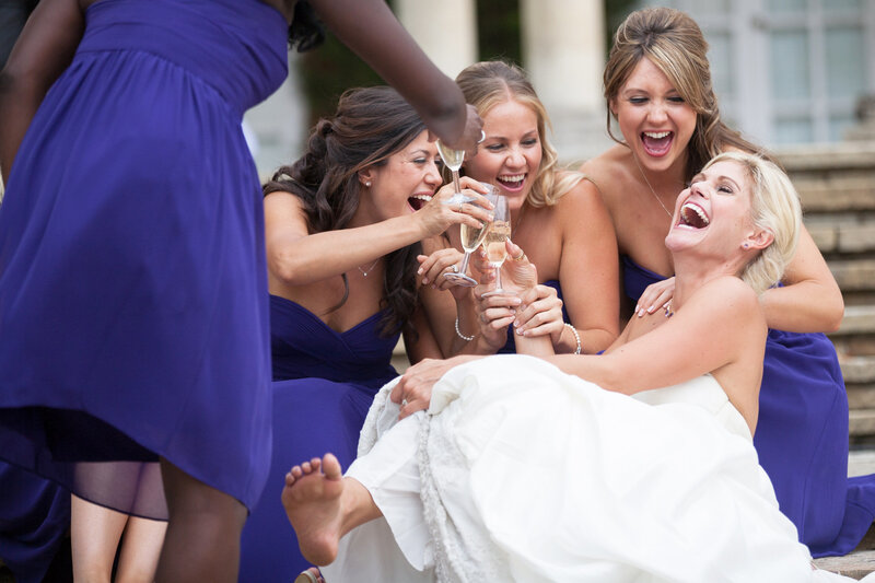 Bride laughing with bridesmaids and champagne classes on steps