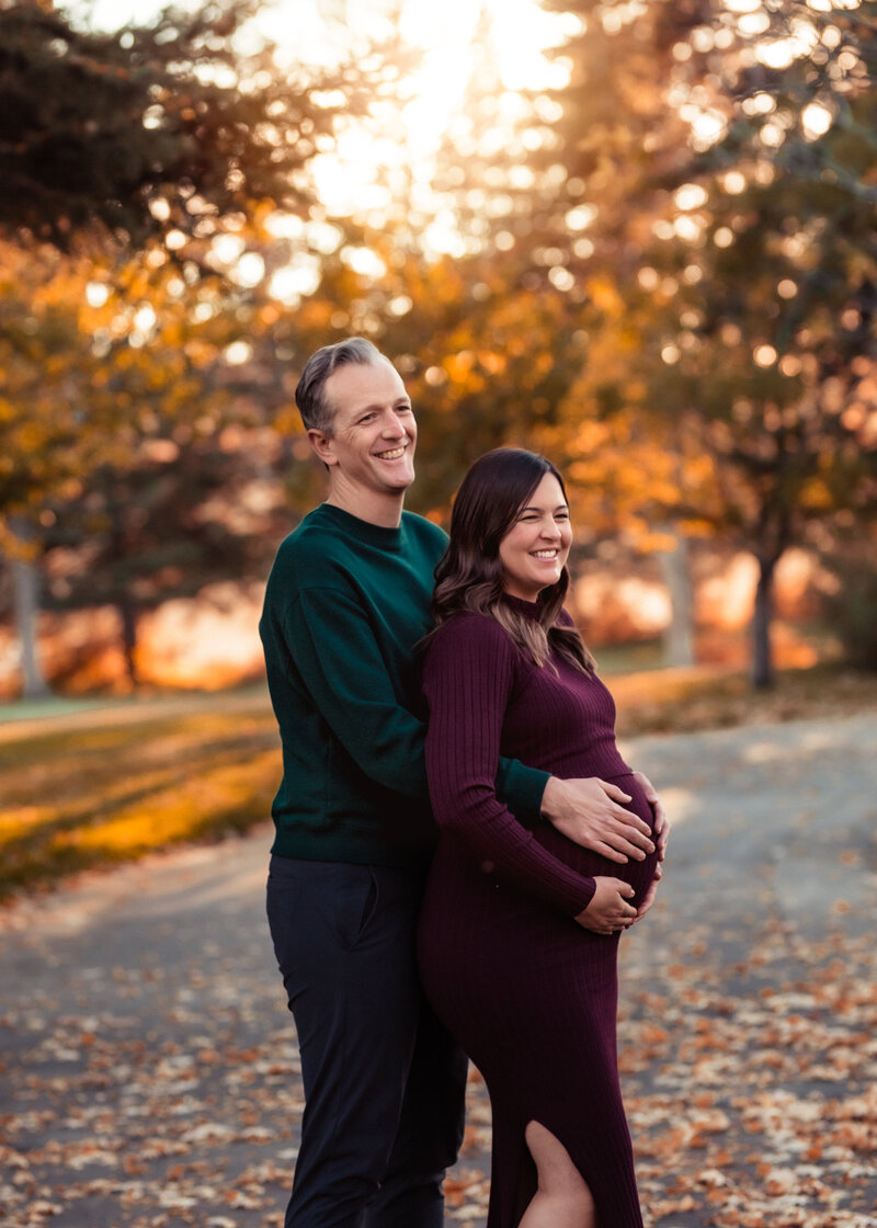 Pregnant woman in maroon with husband in green smiling outside
