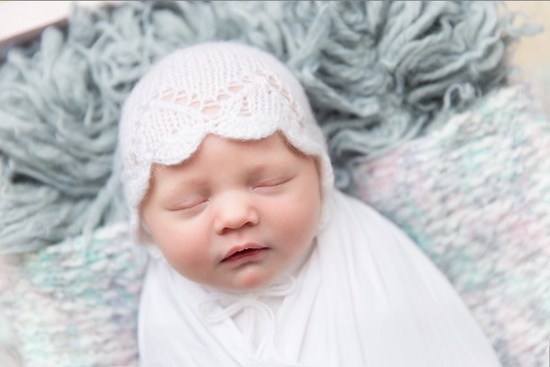 white wrapped newborn with white bonnet