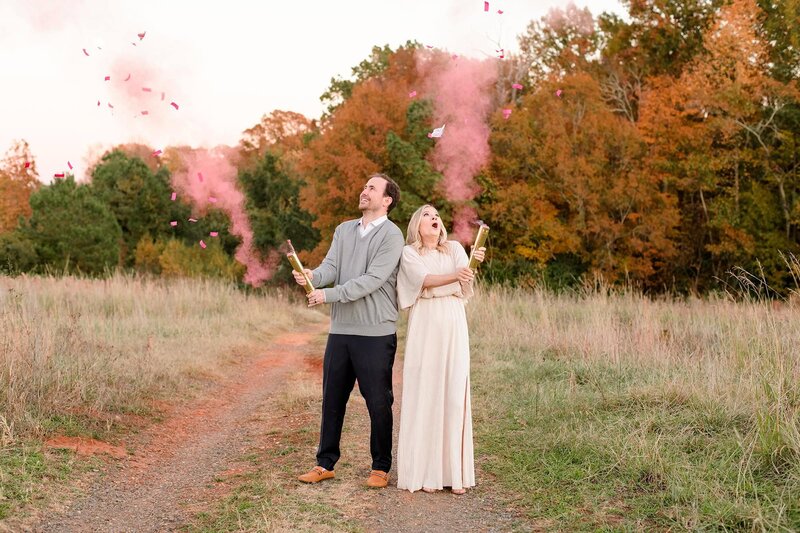 couple at gender reveal with pink smoke in the air as part of their charlotte maternity session