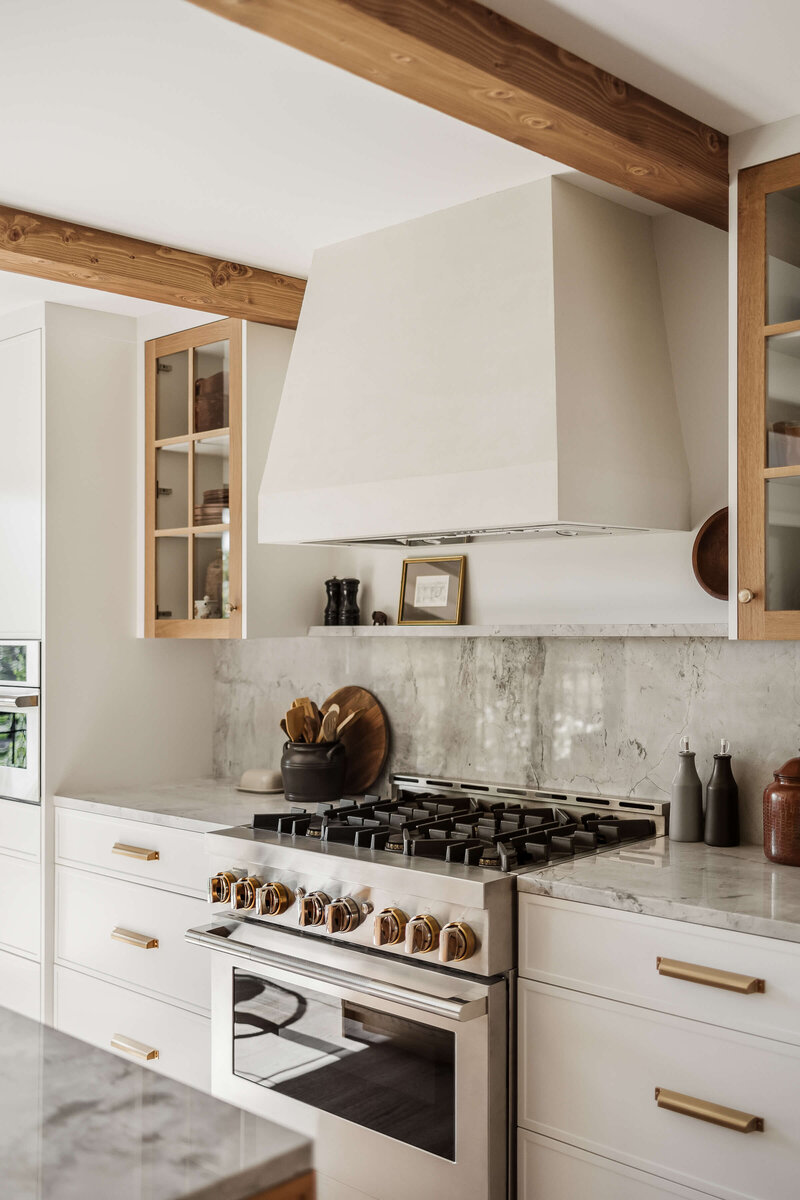 traditional stage home with light filled room including six panelled windows and glass circular table with solid carved wood bottom, built in book shelves along white painted walls and modern white sculptural vase filled with green branches