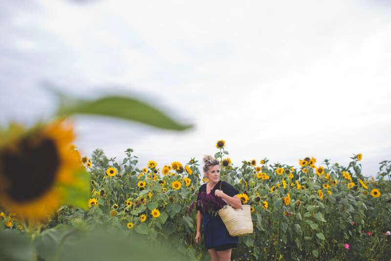 women holding a back while standing in a field of sunflowers