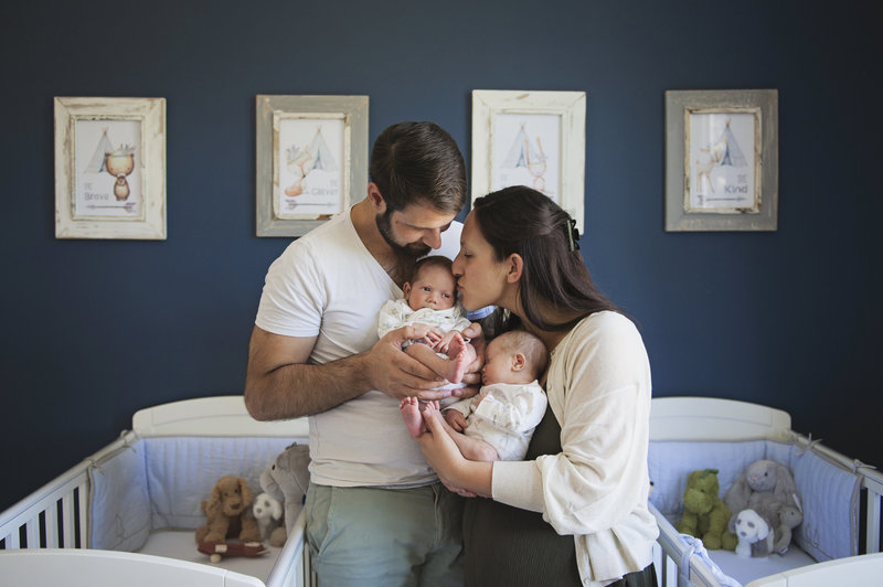 Mother and father holding and kissing their newborn baby boys in their nursery