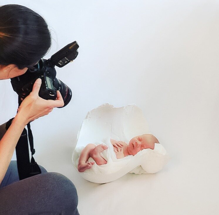 Behind the scenes as Charlotte newborn photographer Alicia Insley Smith captures a photo of a peacefully sleeping newborn baby boy, wrapped in white and nestled in mom's belly cast as a prop.