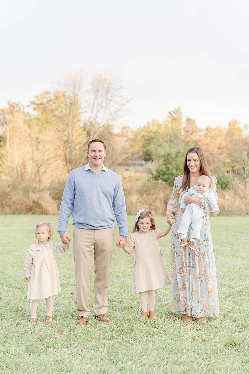 family of 4 holding hands posing for photos during fall minis in Loudoun County, Virginia