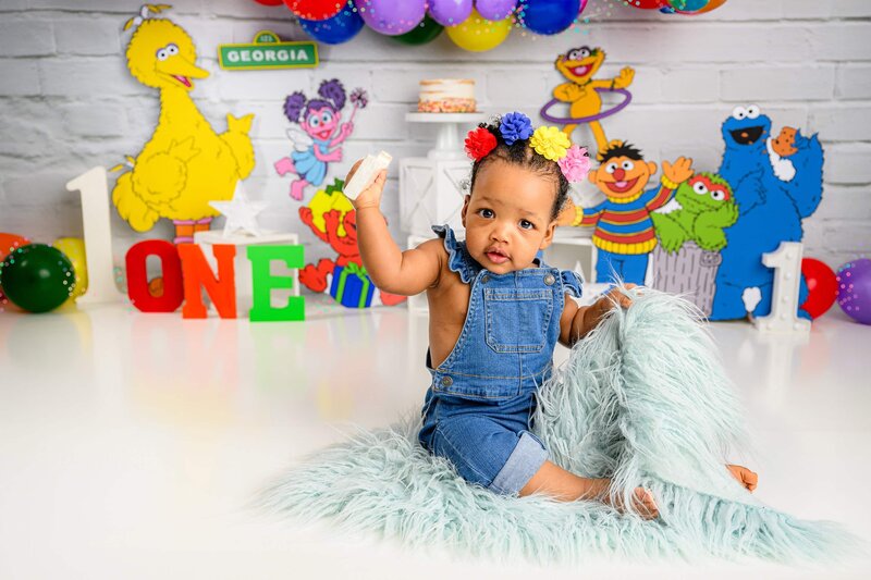 ome year old girl sits in overalls in a sesame street cake smash set
