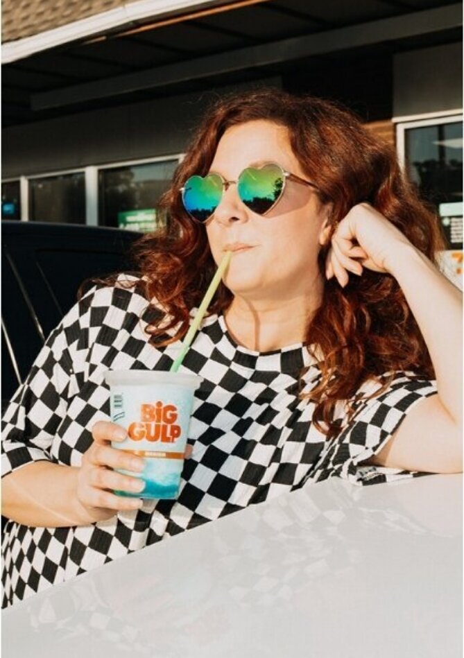 A woman sipping a slurpee and leaning against a cars