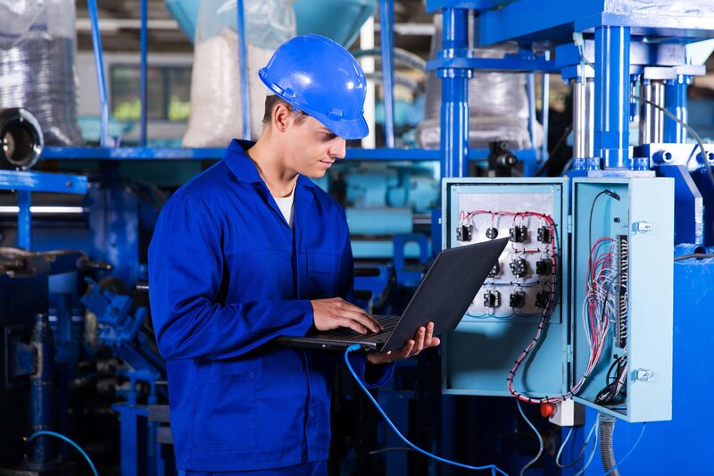 Trained engineer wearing blue checking a manufacturing machine