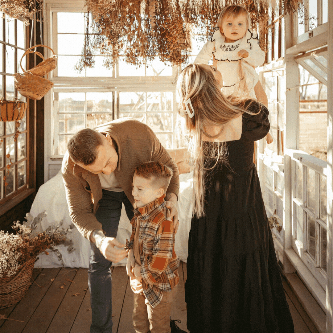 Family photography session in a greenhouse. Watch as parents play with their kids, creating heartwarming moments. Dressed in beautiful flower dresses, beige pants, and comfortable t-shirts, this family radiates joy.