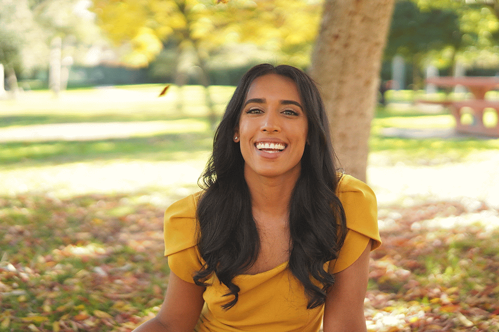 Tania in a yellow dress, smiling at the camera, while leaves are falling around her