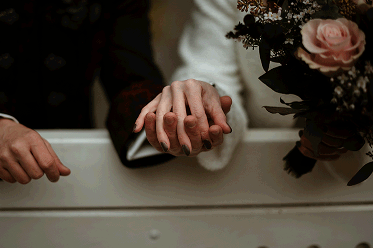 Bewegte Detailaufnahme der miteinander spielenden Hände eines Brautpaares.