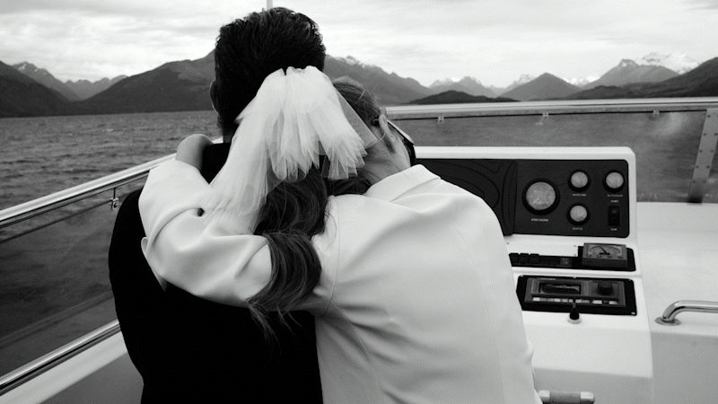 The Lovers Elopement Co - bride and groom embrace on boat in Queenstown lake with wind moving the bride's veil